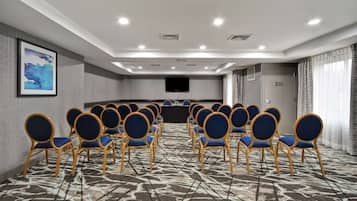 A conference room with rows of blue chairs, a large screen, and a patterned carpet.