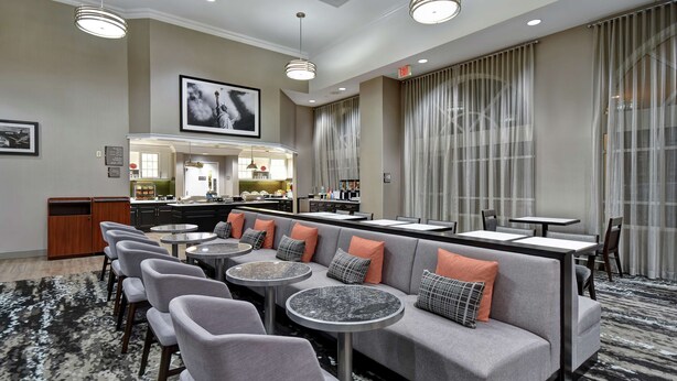 A modern hotel lobby with a seating area, a bar, and a kitchen in the background. - Homewood Suites by Hilton Edgewater (Edgewater)
