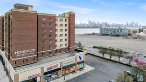 A hotel with multiple floors, a parking lot, and a view of a city skyline. - Homewood Suites by Hilton Edgewater (Edgewater)