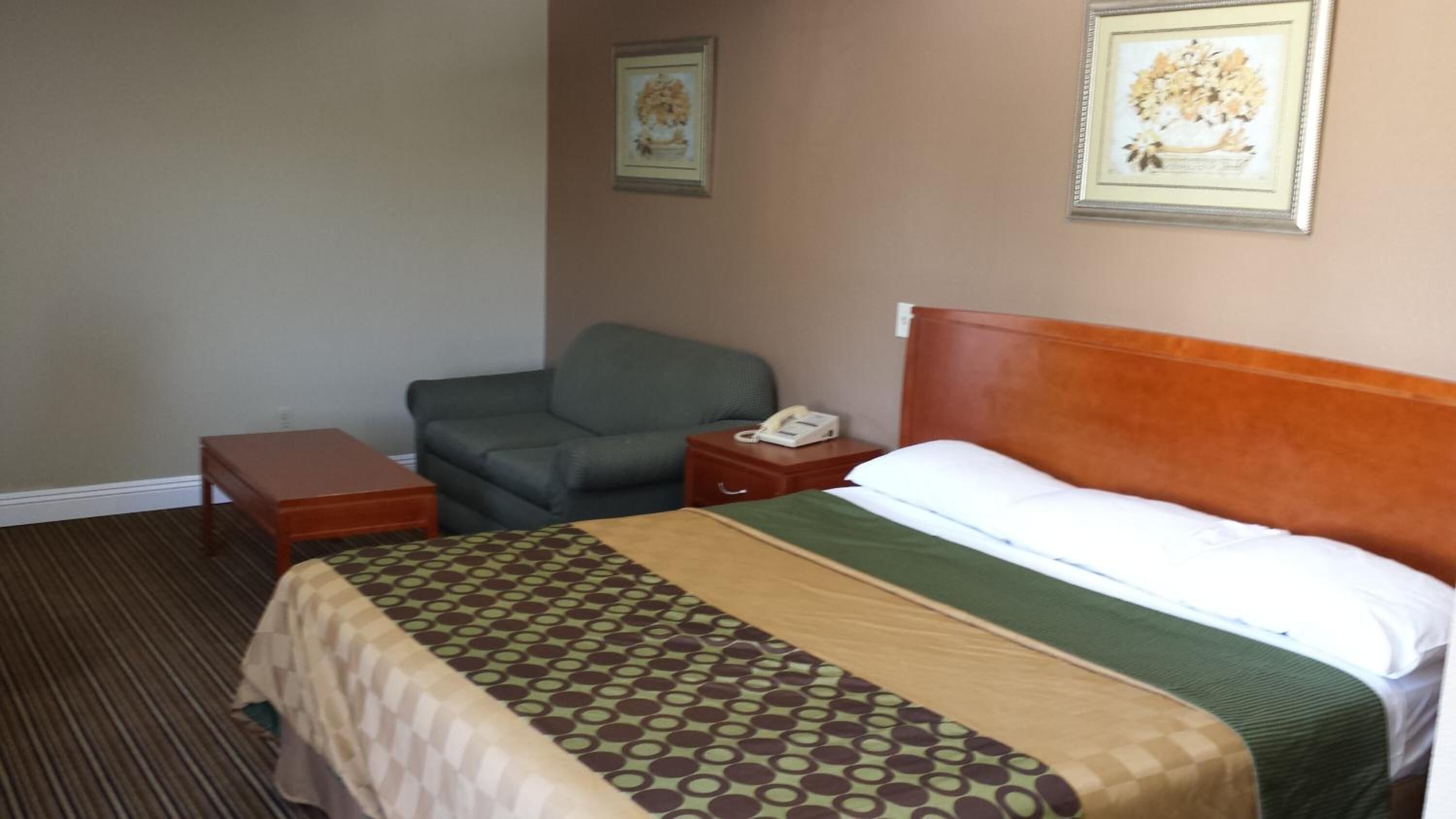 A hotel room with a bed, a chair, a nightstand, and a telephone.