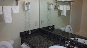 A bathroom with a granite countertop, a white sink, a mirror, and two hair dryers mounted on the wall.