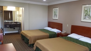 A hotel room with two beds, a bathroom with a sink, and a mirror.