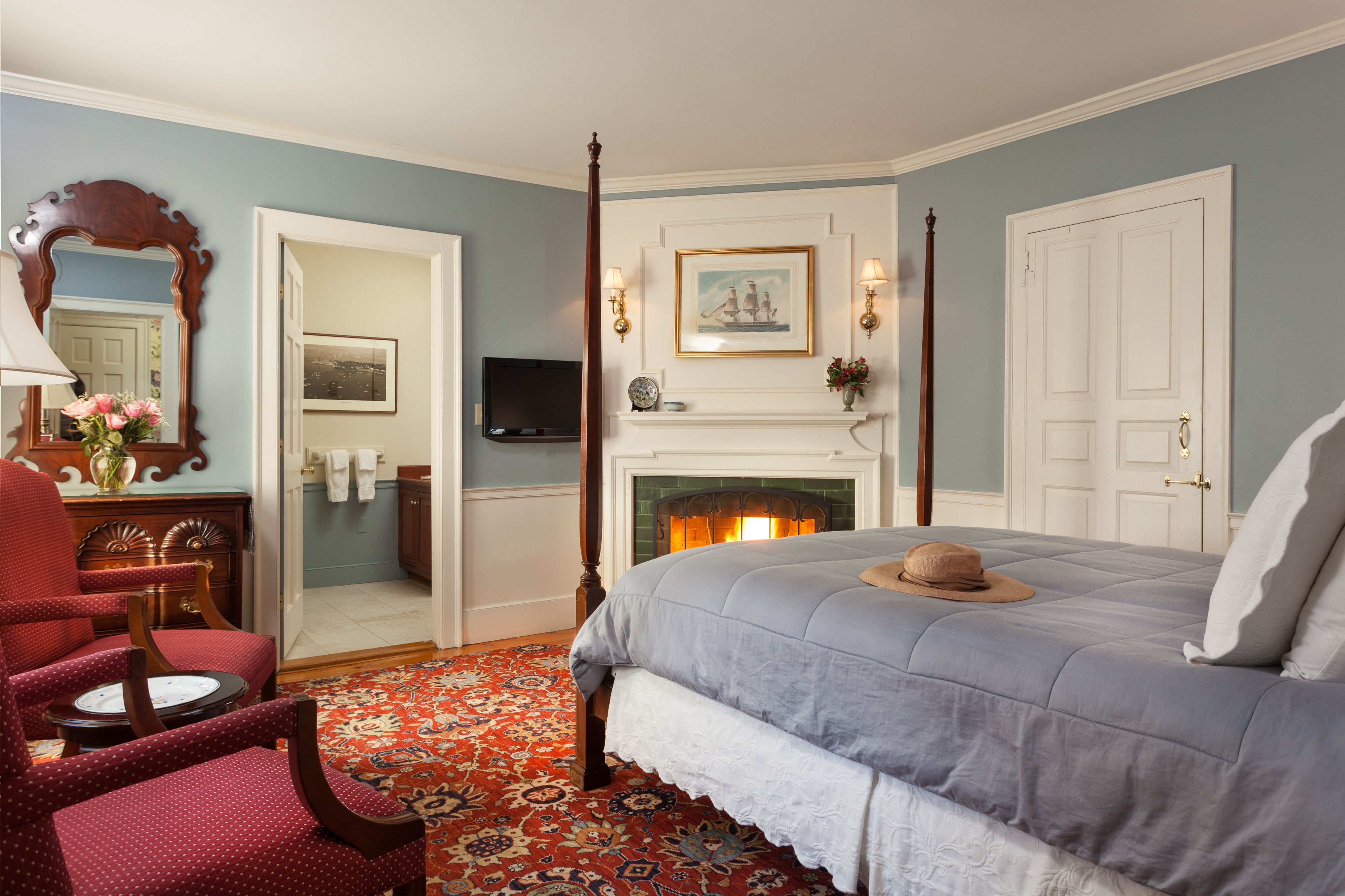 Une chambre à coucher avec un lit à baldaquin, une cheminée, un téléviseur et un tapis rouge à motifs.