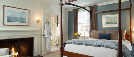 A four-poster bed with a floral bedspread, a fireplace, and a framed seascape painting on the wall.