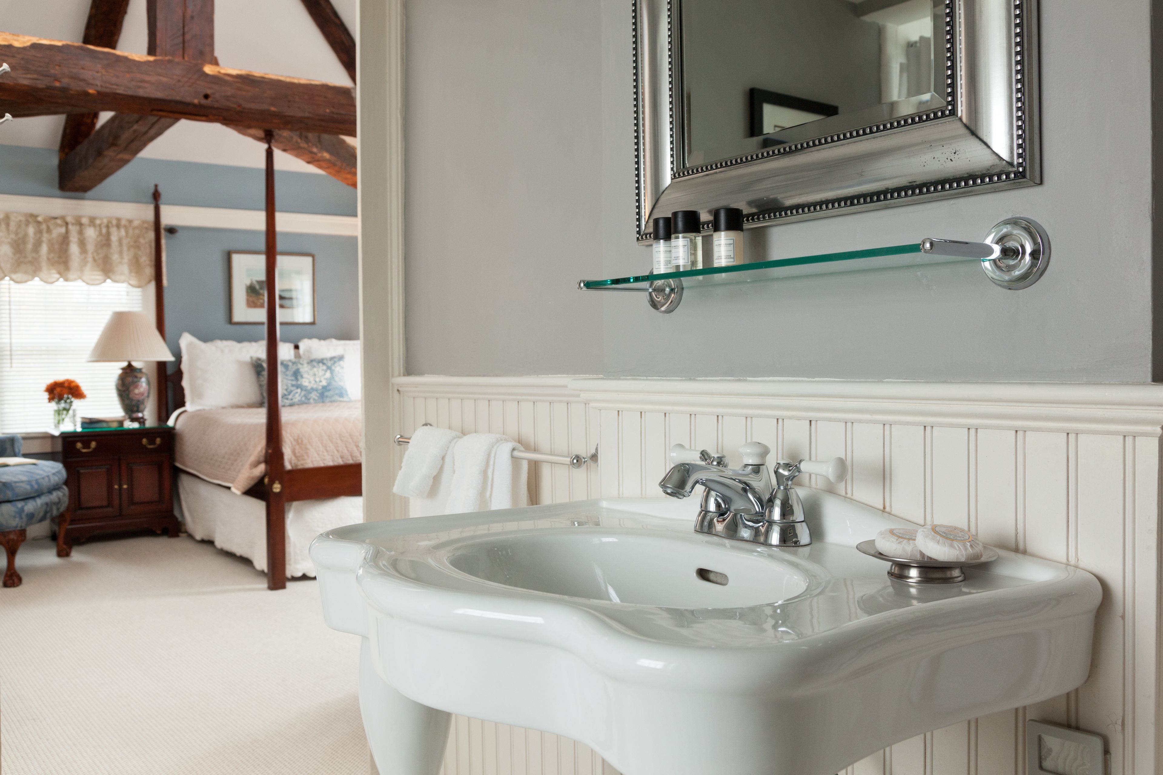 A bathroom with a white sink, a mirror, and a glass shelf above the sink.
