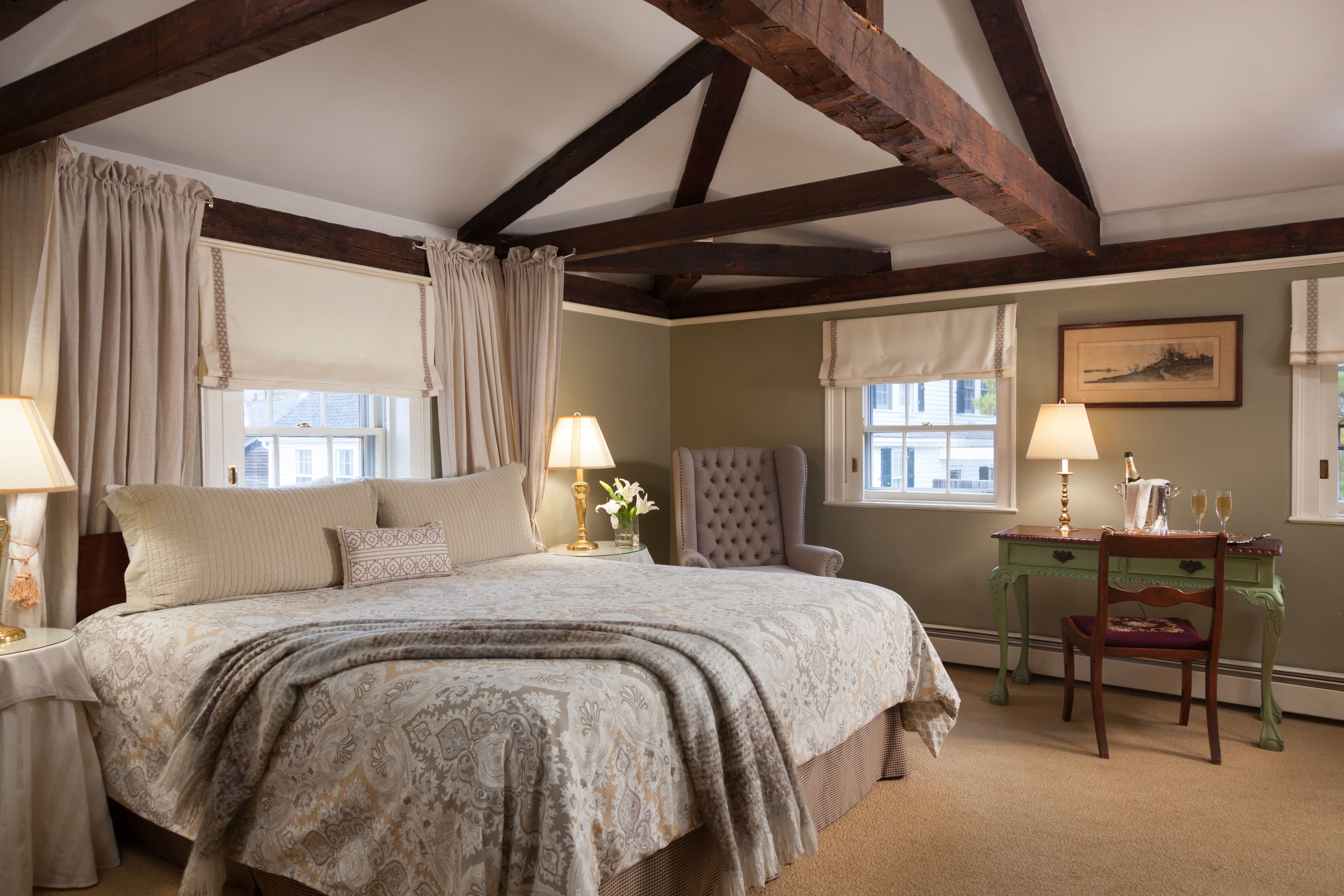 A bedroom with a large bed, two bedside tables with lamps, a green desk with a chair, and a framed picture on the wall.