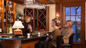 A bar area with a wine rack, bottles, and glasses. There are three people seated at the bar. - Harbor Light Inn (Marblehead)