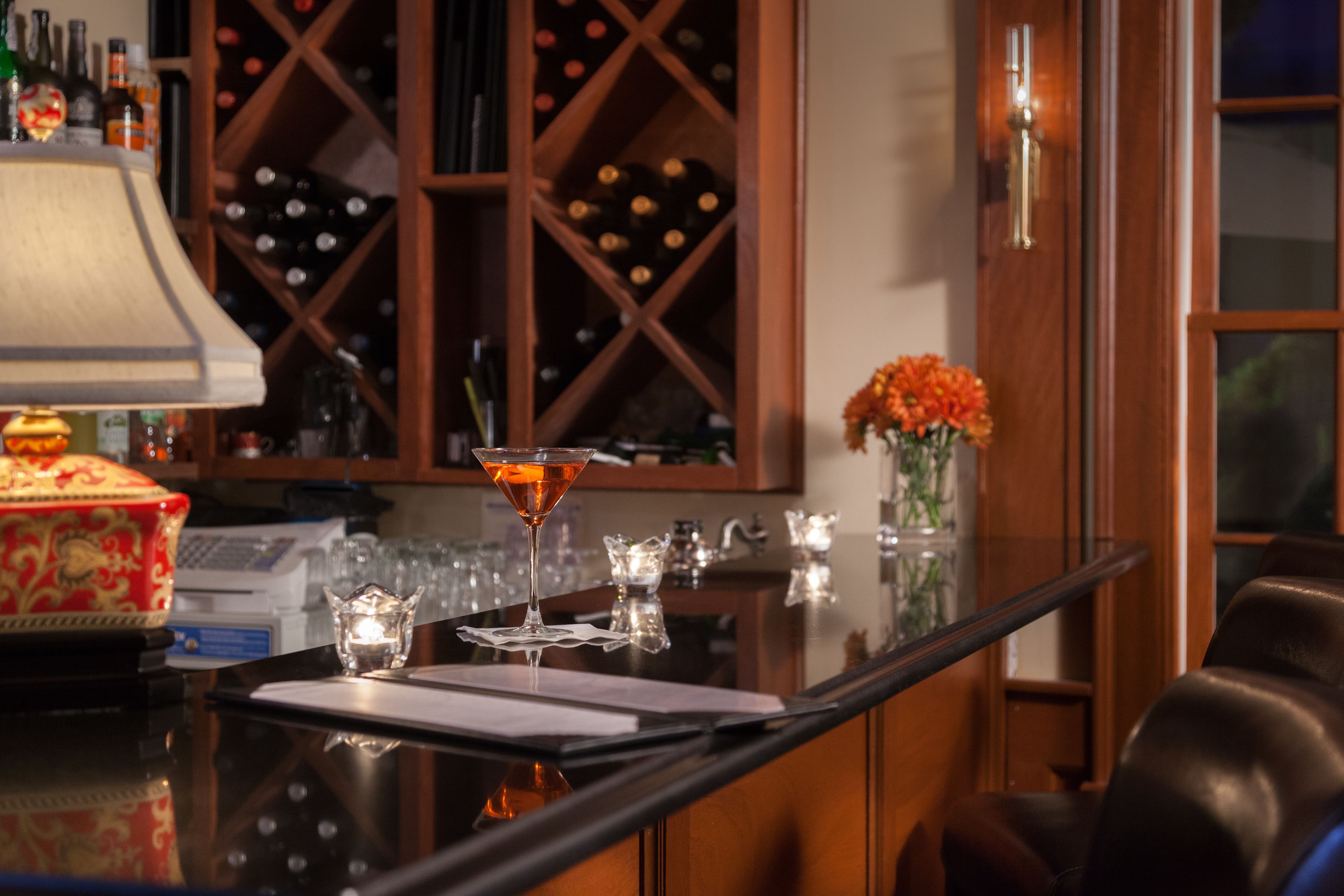 A bar area with a wine rack, a vase with flowers, and a martini glass on a reflective surface.