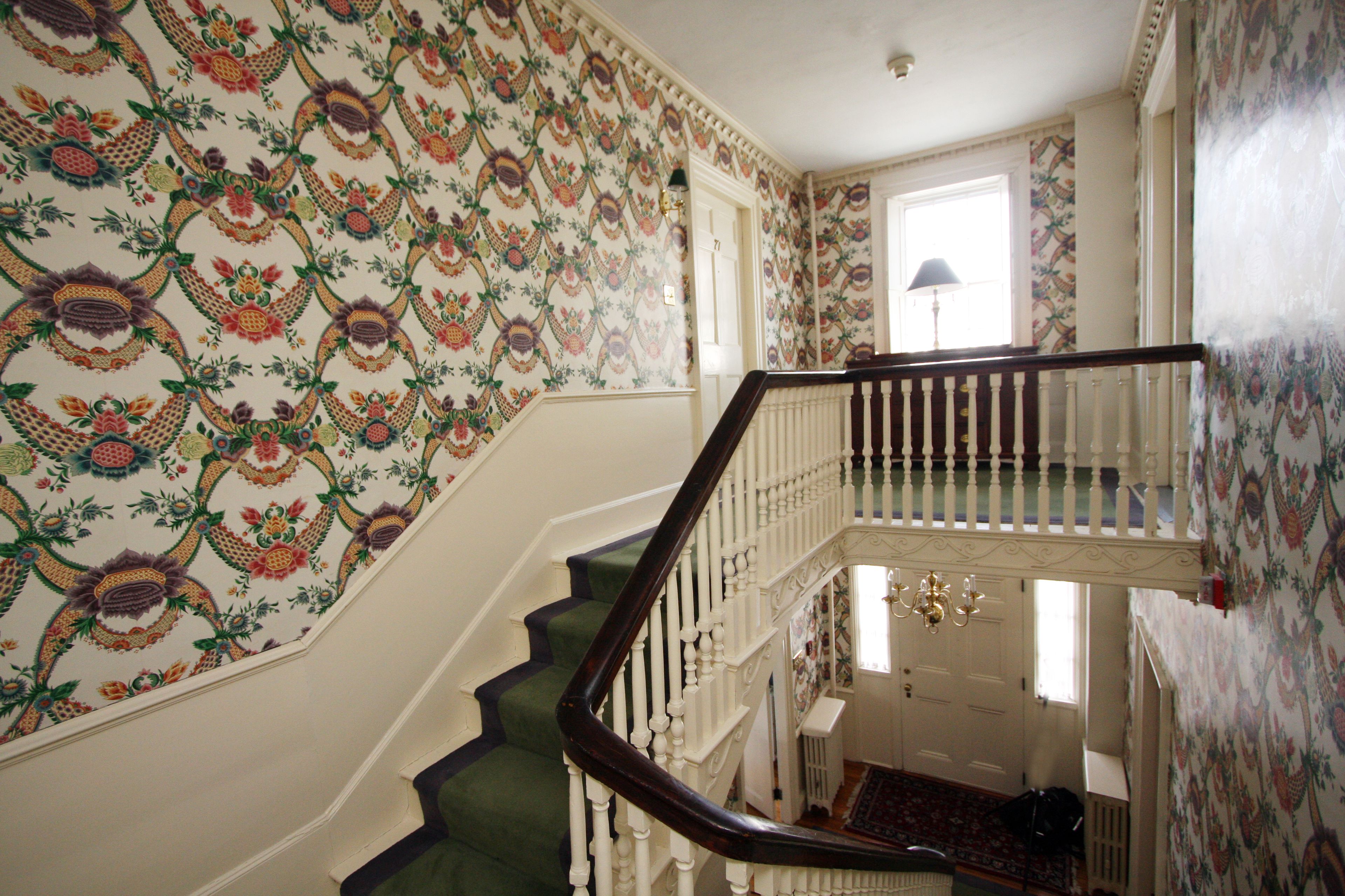 A staircase with ornate wallpaper and a chandelier.