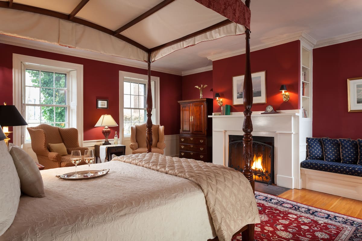 A bedroom with a large bed, a fireplace, a sitting area with a sofa, and a dining table with wine glasses.