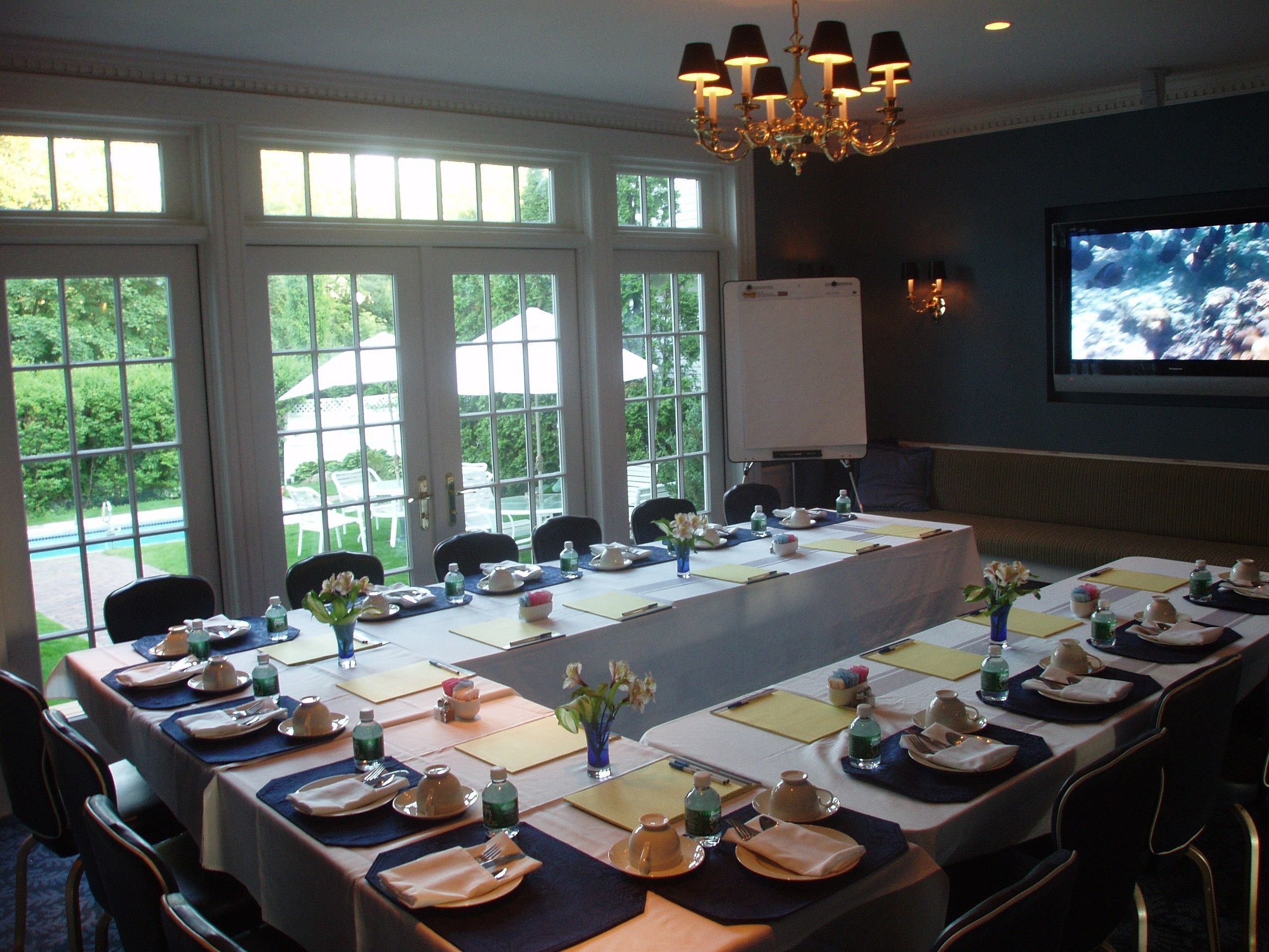 A conference room with a long table set for a meeting, large windows, and a projector screen.