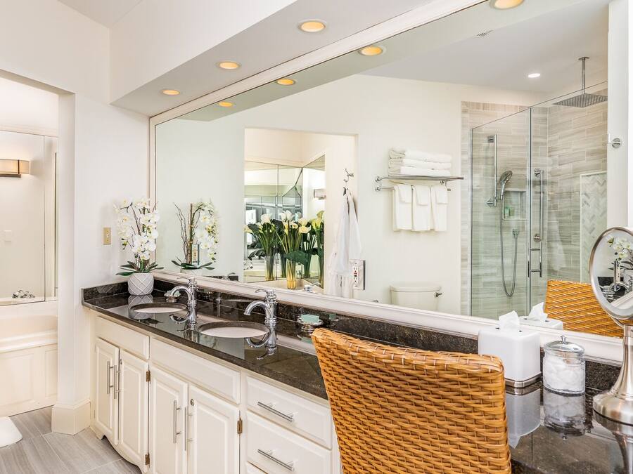 A modern bathroom with a large mirror, two sinks, a shower, and wicker chairs.