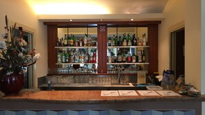 Una zona de bar con estantes llenos de botellas de licores, vasos y un jarrón grande con flores.