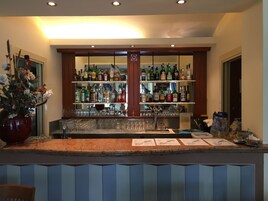 Una zona de bar con estantes llenos de botellas de licores, vasos y un jarrón grande con flores.