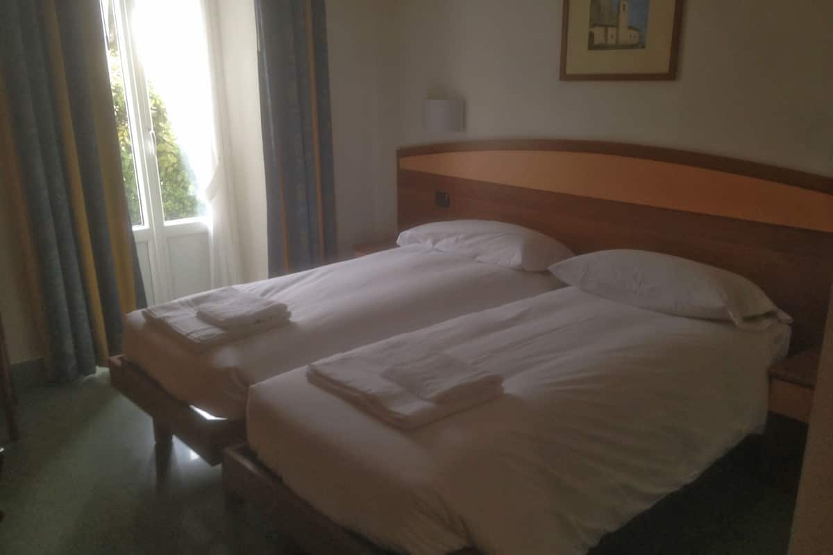 A double bed with white linens and towels, a wooden headboard, and a window with curtains.