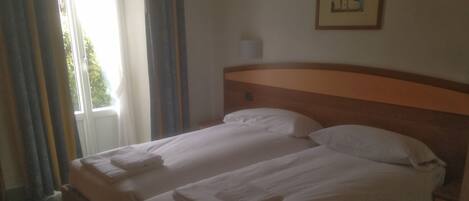 Una cama doble con ropa de cama y toallas blancas, un cabecero de madera y una ventana con cortinas.