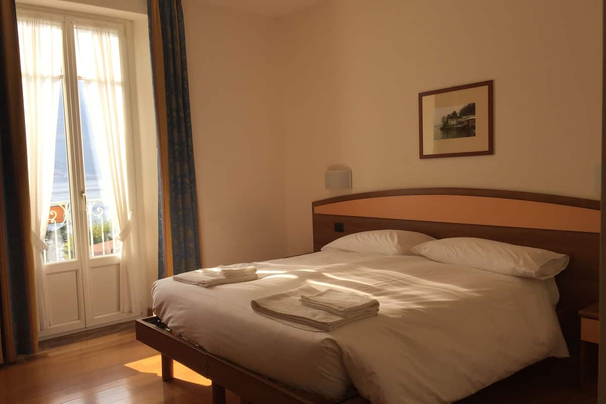 A neatly made bed with white linens and a folded towel on the footboard. A framed picture hangs on the wall above the bed.