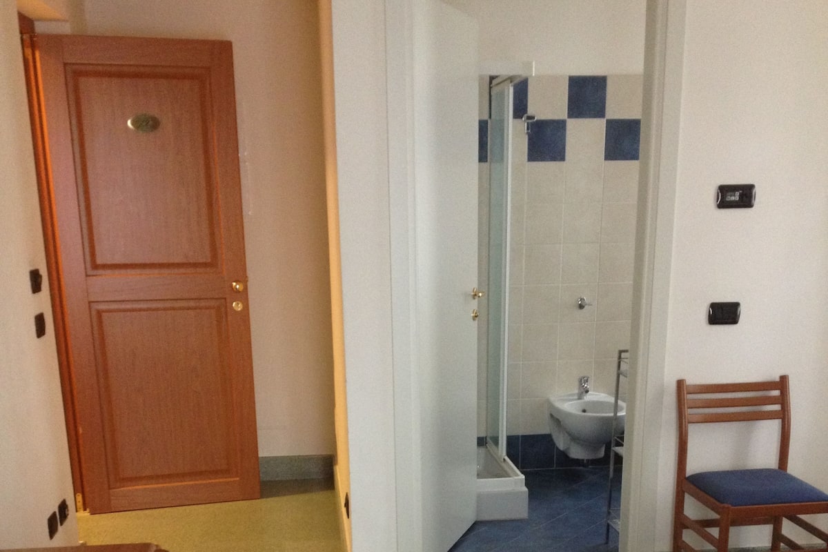 A hotel room with a bed, a wooden desk, a chair, and a bathroom visible through an open door.