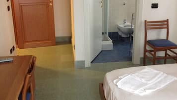 A hotel room with a bed, a wooden desk, a chair, and a bathroom visible through an open door.