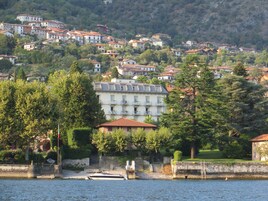 Un pueblo junto al lago con edificios en una ladera, un muelle con un bote y un muro de piedra a lo largo del agua.
