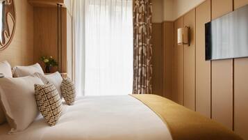 A hotel room with a large bed, a flat-screen TV mounted on the wall, and a window with sheer curtains.