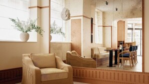 A spacious living area with a beige sofa, a dining table with chairs, and a large window with plants. - Vintimille Hotel (Paris)