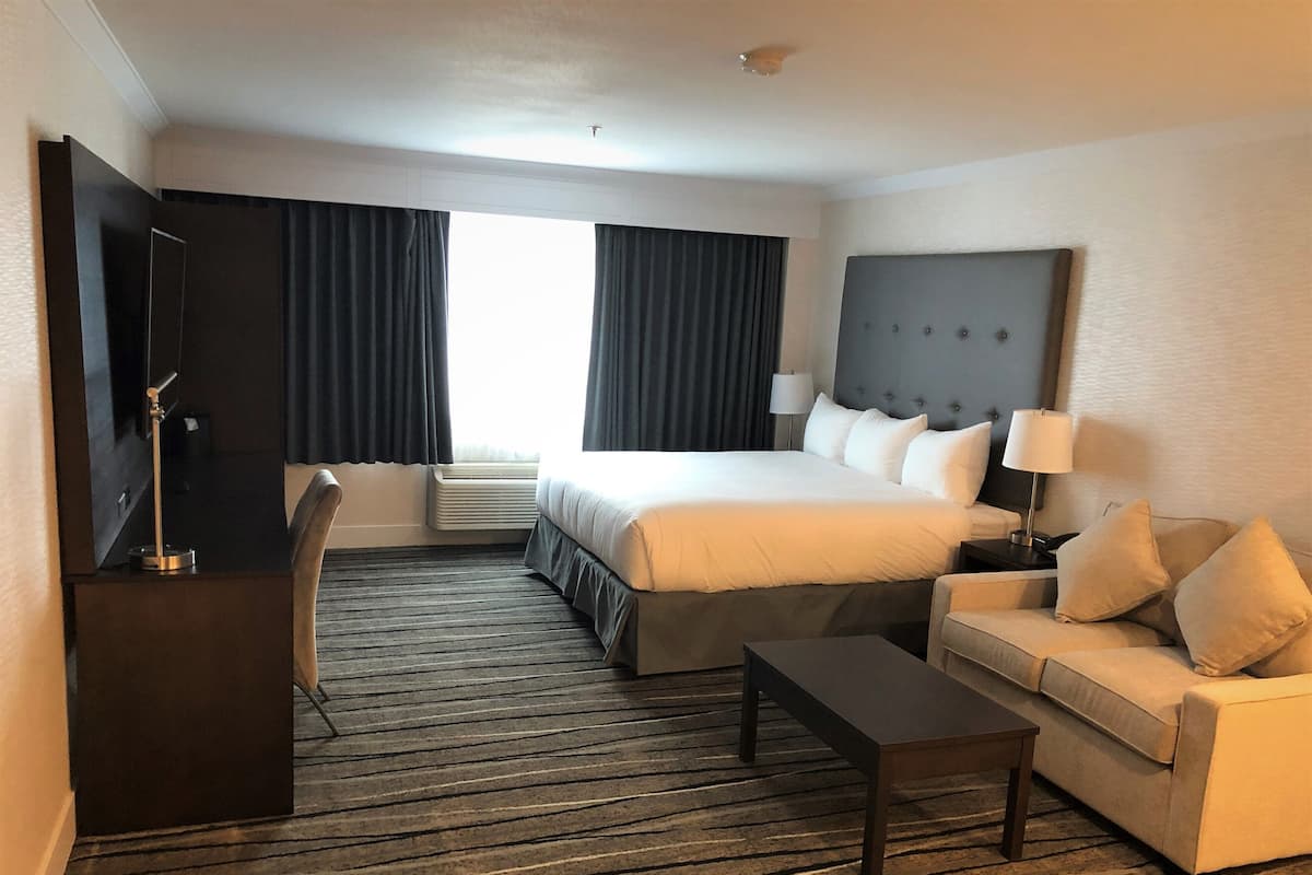 A hotel room with a large bed, a sofa, a desk, and a TV.