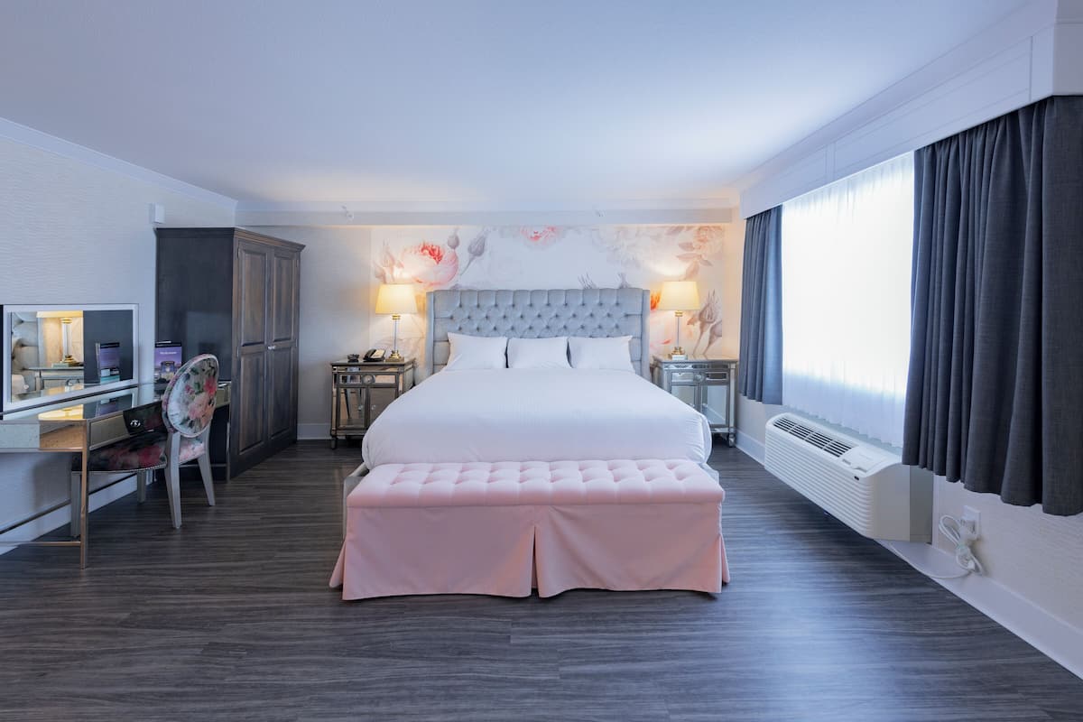 A hotel room with a large bed, a desk with a chair, a wardrobe, and a window with curtains.