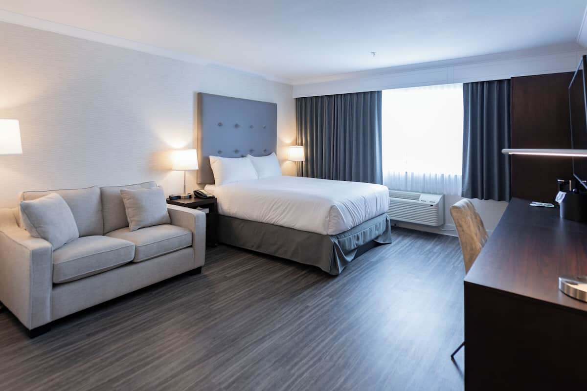 A hotel room with a bed, a sofa, a desk, and a large window with curtains.