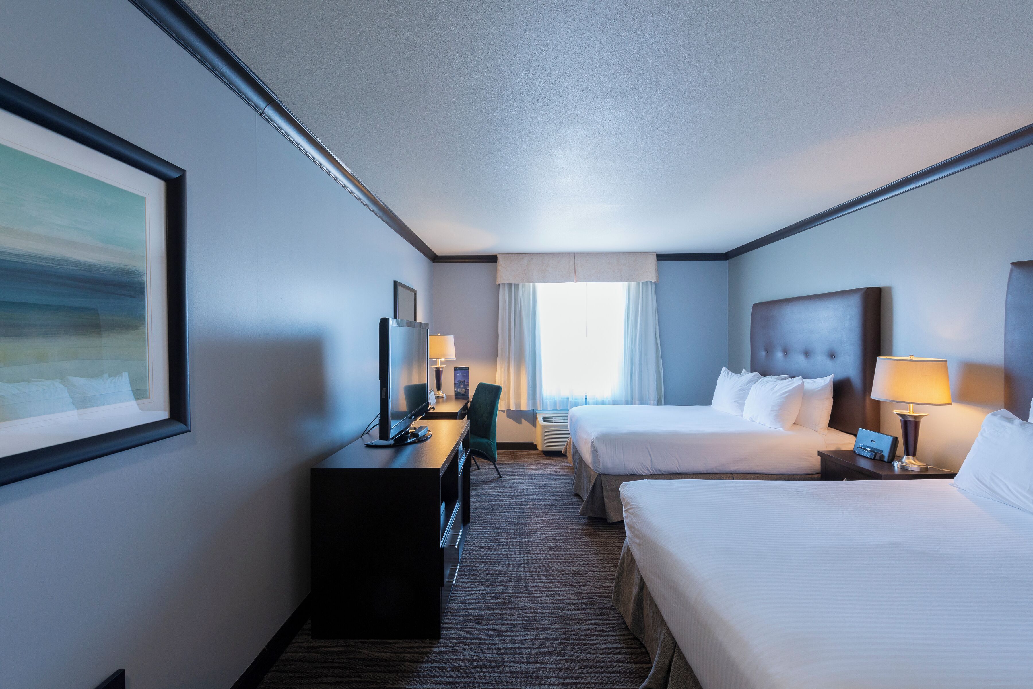 A hotel room with two beds, a desk, a chair, a TV, and a window with curtains.