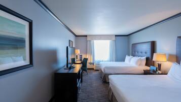 A hotel room with two beds, a desk, a chair, a TV, and a window with curtains.