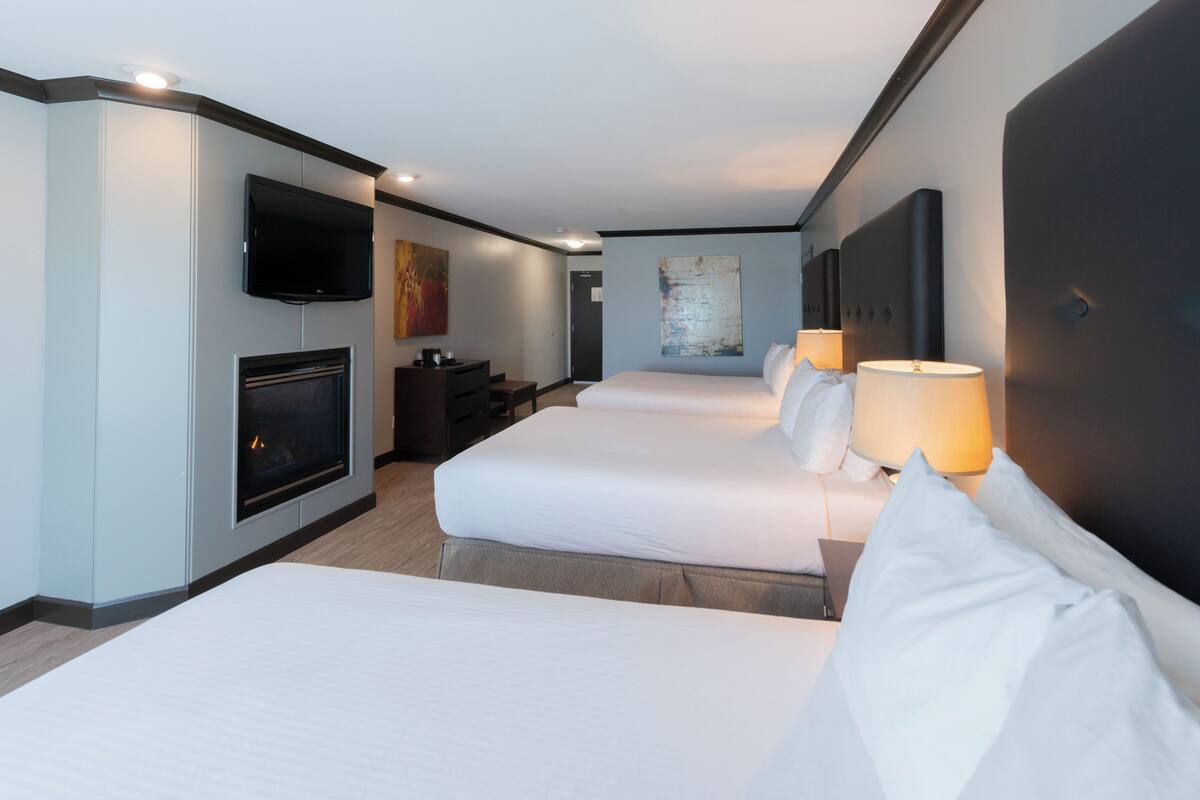 A hotel room with two beds, a flat-screen TV, a fireplace, and a desk with a lamp.