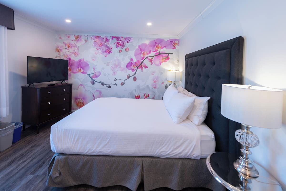A hotel room with a bed, a television on a dresser, and a wall with a floral mural.
