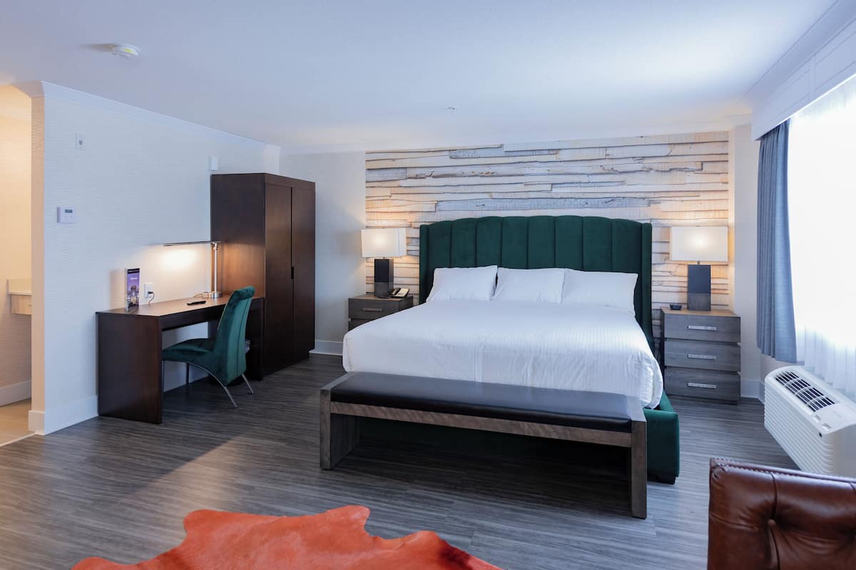 A modern hotel room with a large bed, a desk, a chair, and a bench.