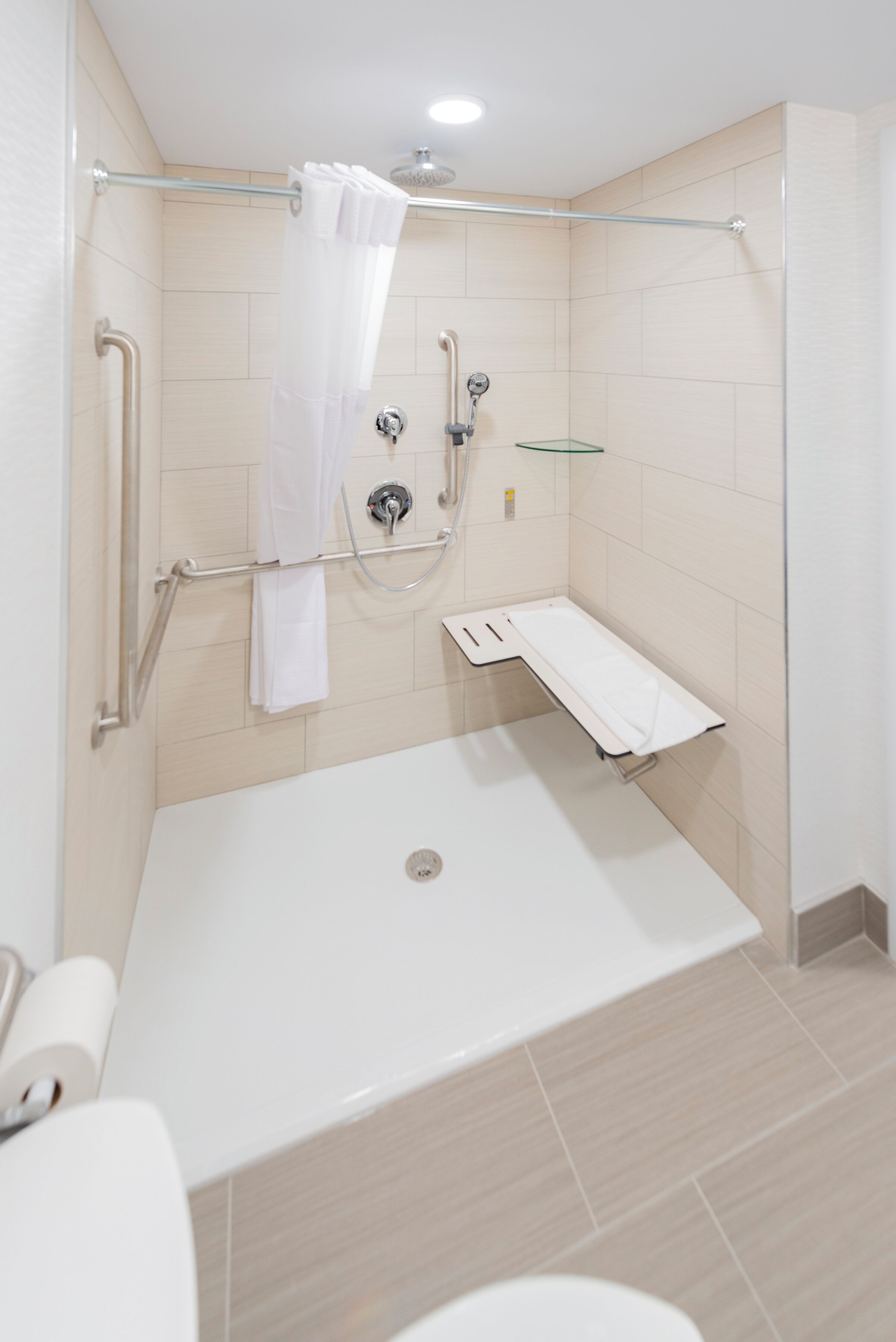 Een moderne badkamer met een inloopdouche, handgrepen, een glazen plank en een witte badkuip.