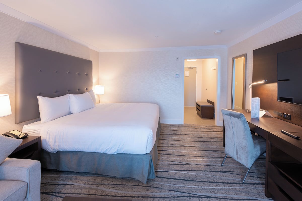 A hotel room with a large bed, a desk with a chair, a television, and a bathroom visible through an open door.