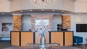 A modern lobby with a central glass table, a chandelier, and a reception desk with wooden accents. - Prestige Treasure Cove Resort (Prince George)