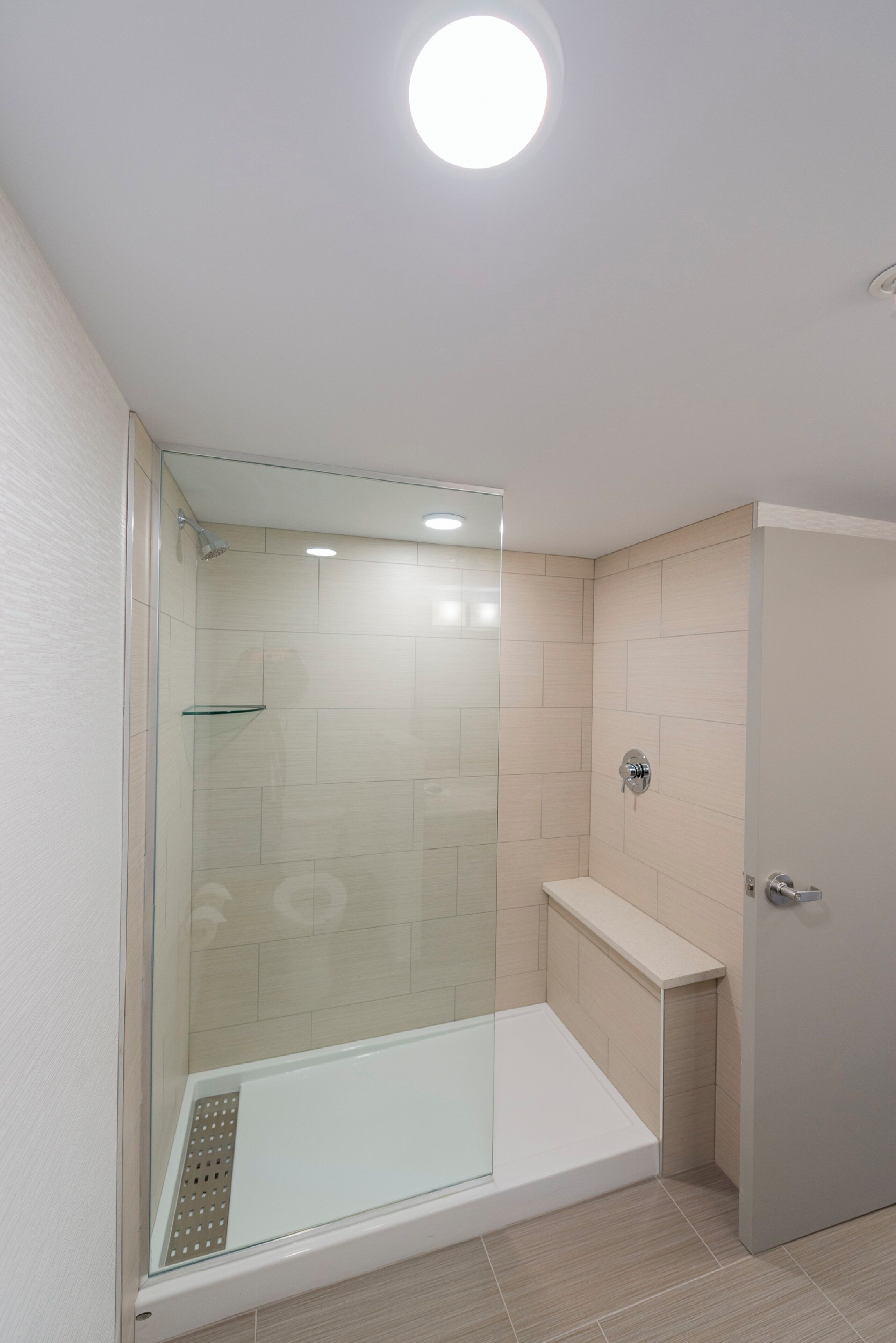A modern bathroom with a glass-enclosed shower, a white sink, and beige tiles.