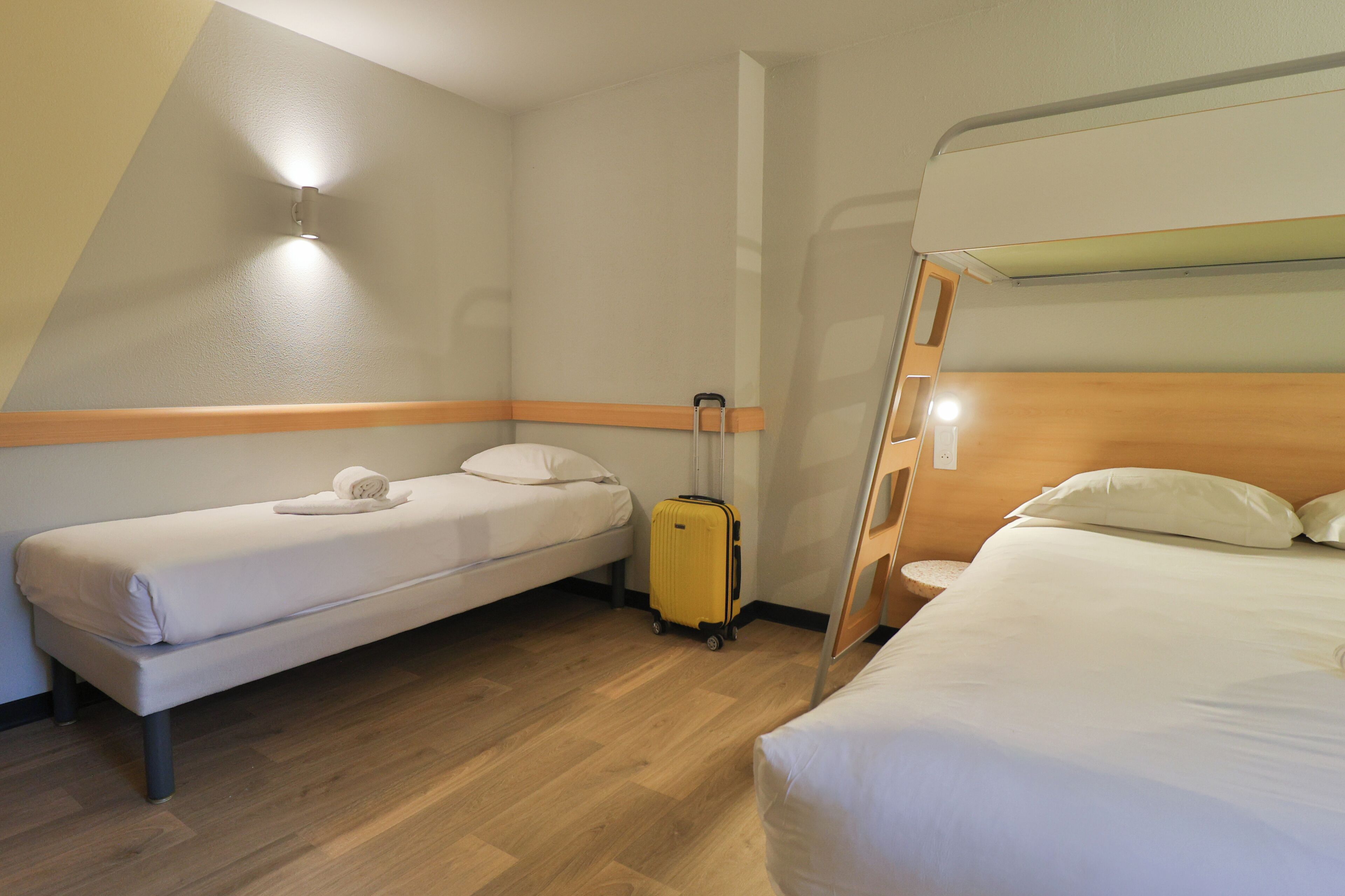 A hotel room with two beds, a wooden floor, and a suitcase.