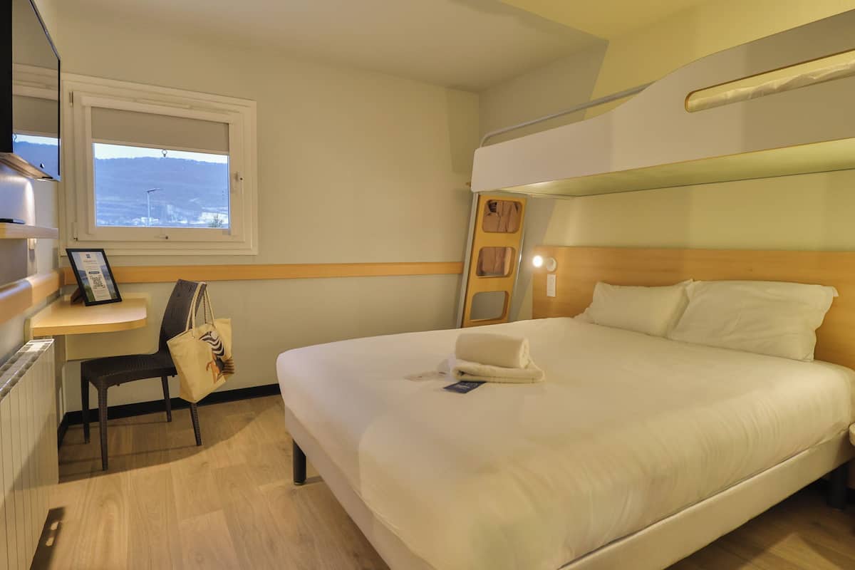 Une chambre d’hôtel avec un lit superposé, un bureau avec une chaise, une fenêtre donnant sur un paysage agréable et une table de chevet.