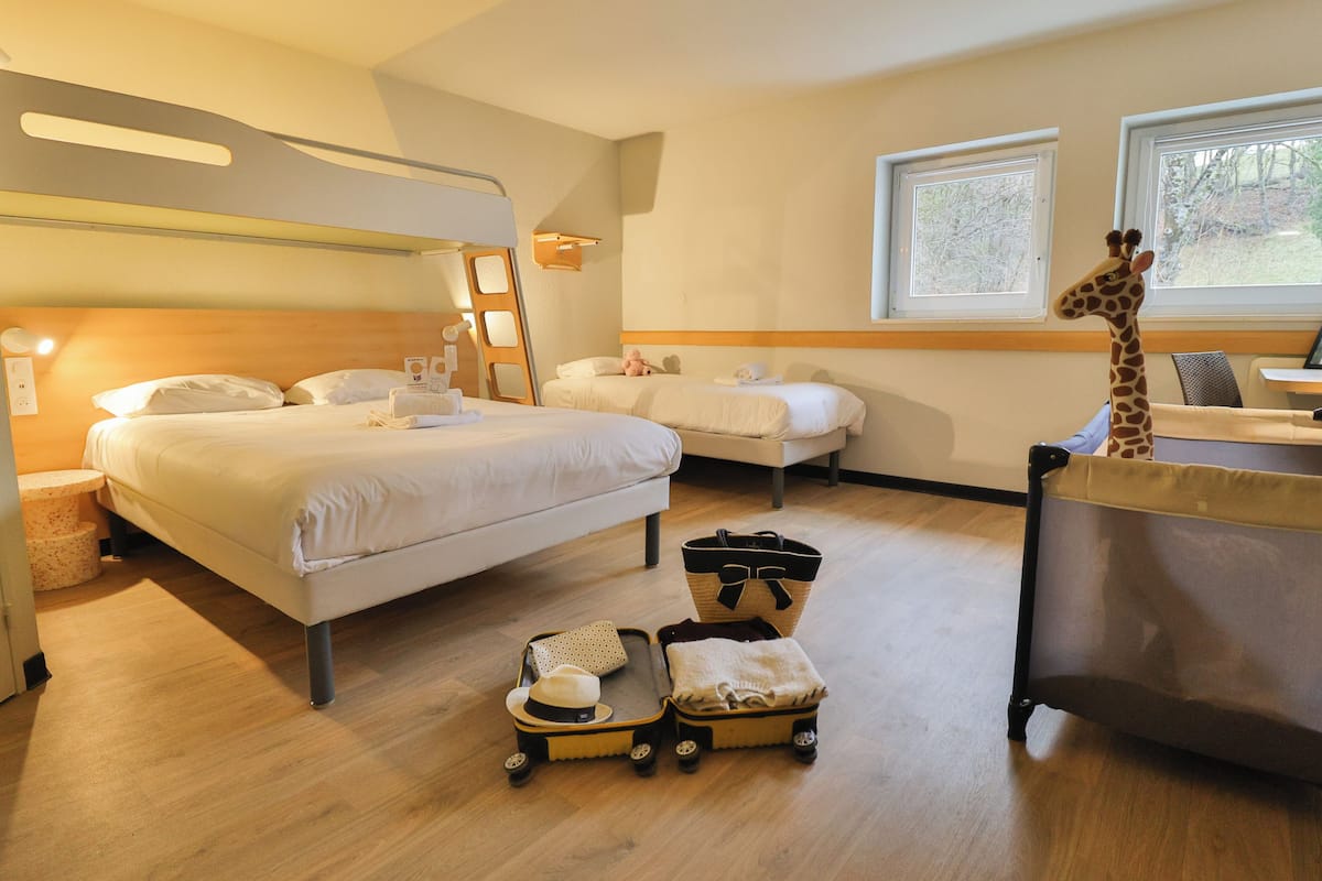 Une chambre d’hôtel avec un lit superposé, un bureau, une chaise, une décoration représentant une girafe et une valise.