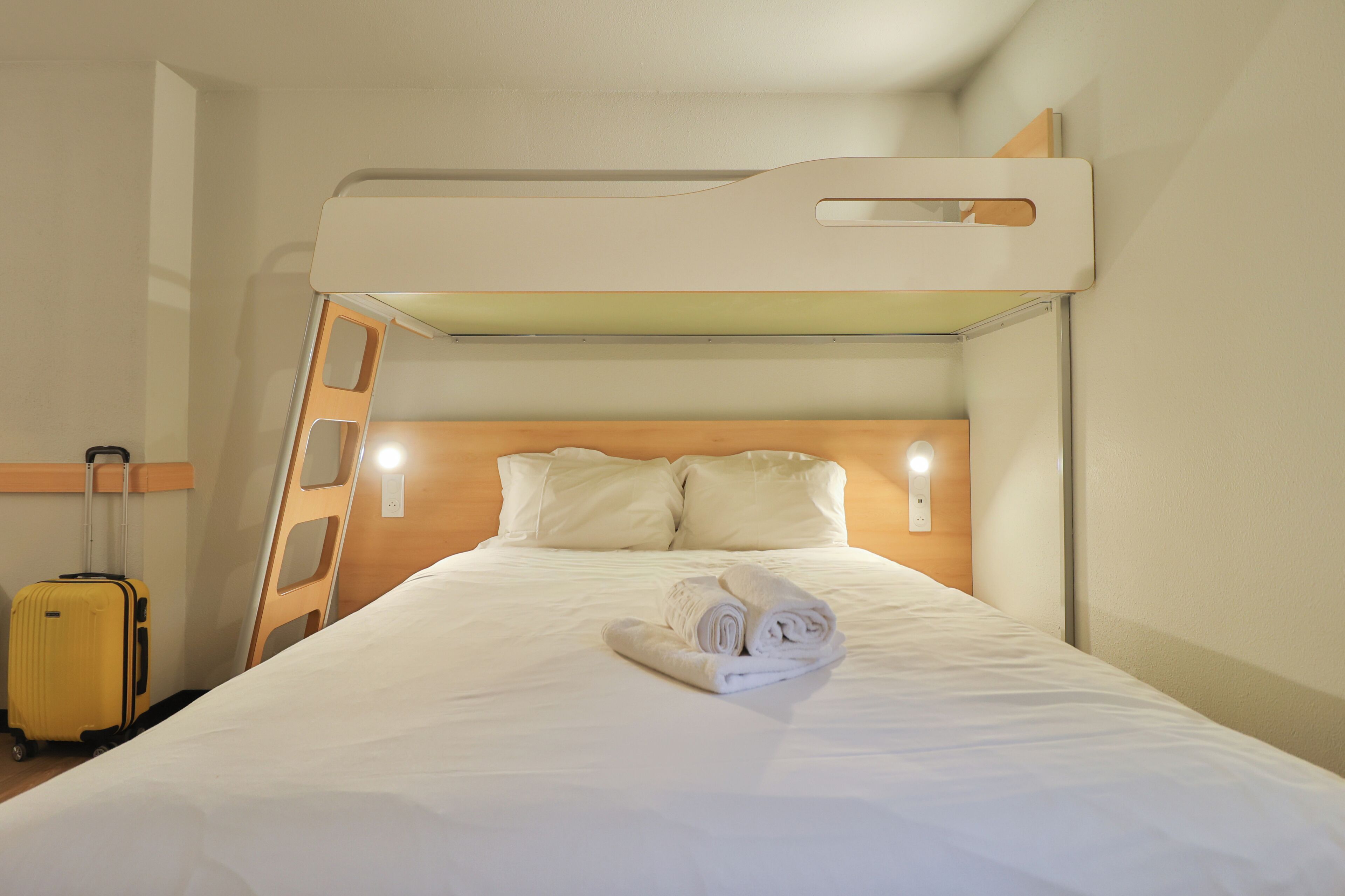 A bunk bed with a ladder, a rolled-up towel, and a suitcase on the floor.