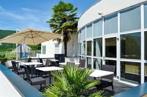 Une terrasse extérieure avec des tables et des chaises, un grand parasol et un palmier.