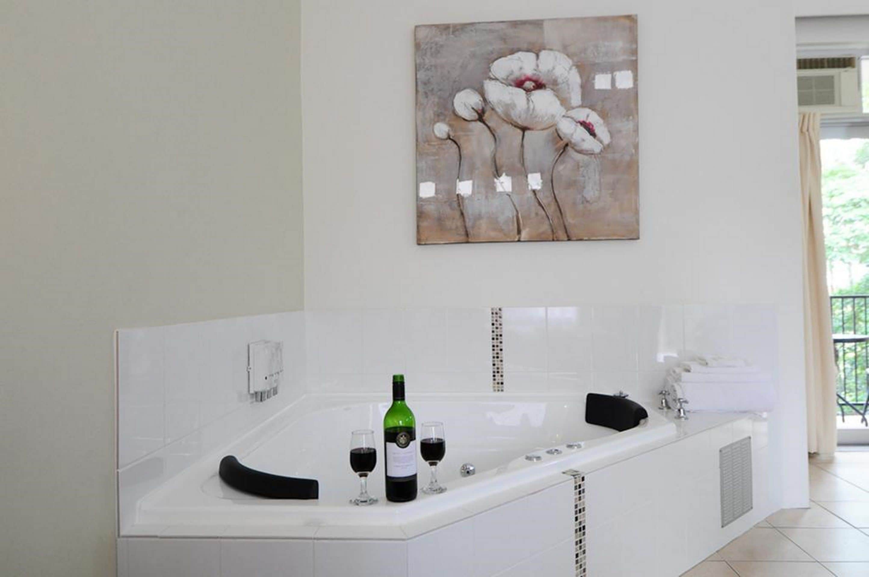 A modern bathroom with a large bathtub, a green bottle of wine, and two glasses of wine.