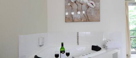 A modern bathroom with a large bathtub, a green bottle of wine, and two glasses of wine.
