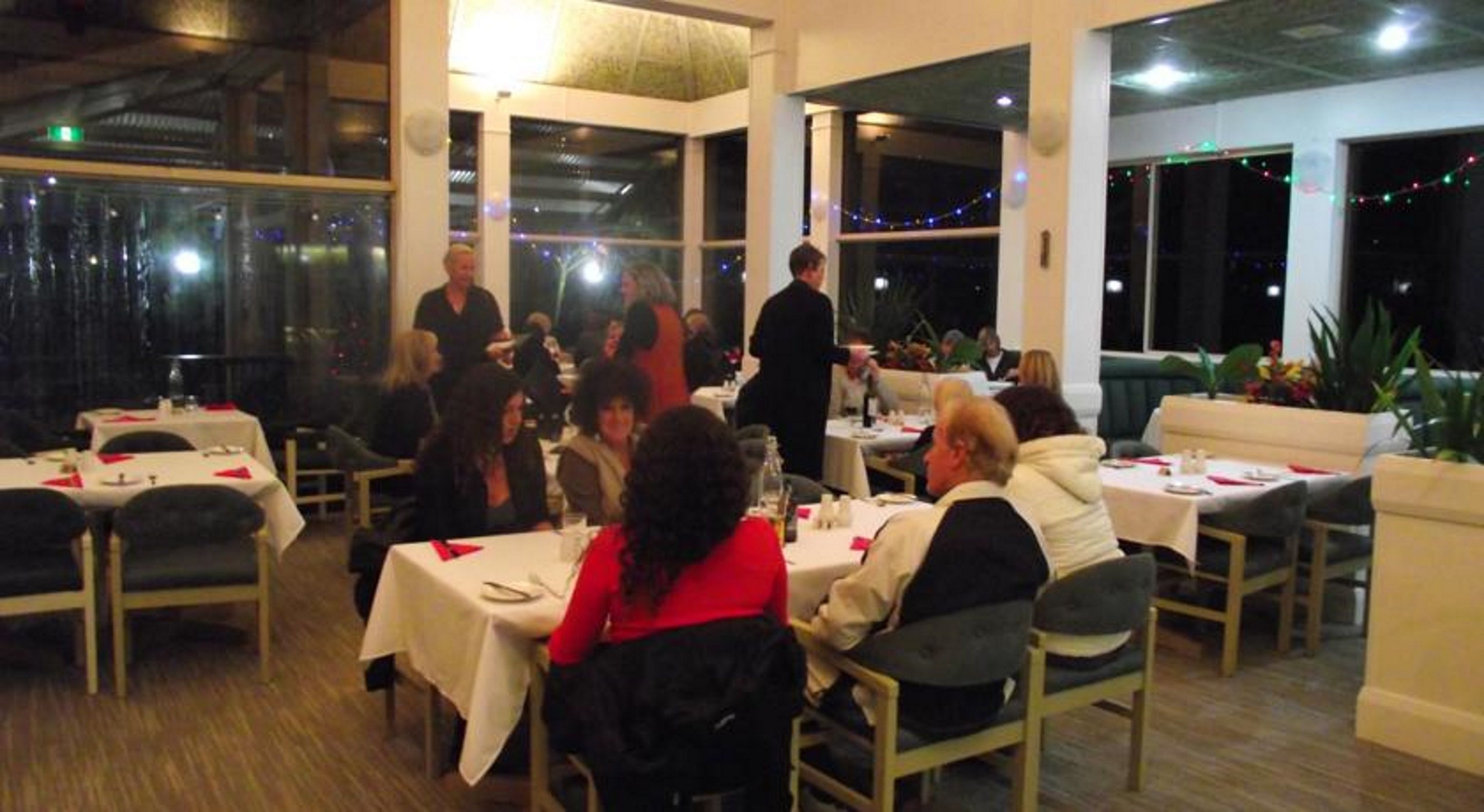A restaurant with tables set for dining, large windows, and indoor lighting.