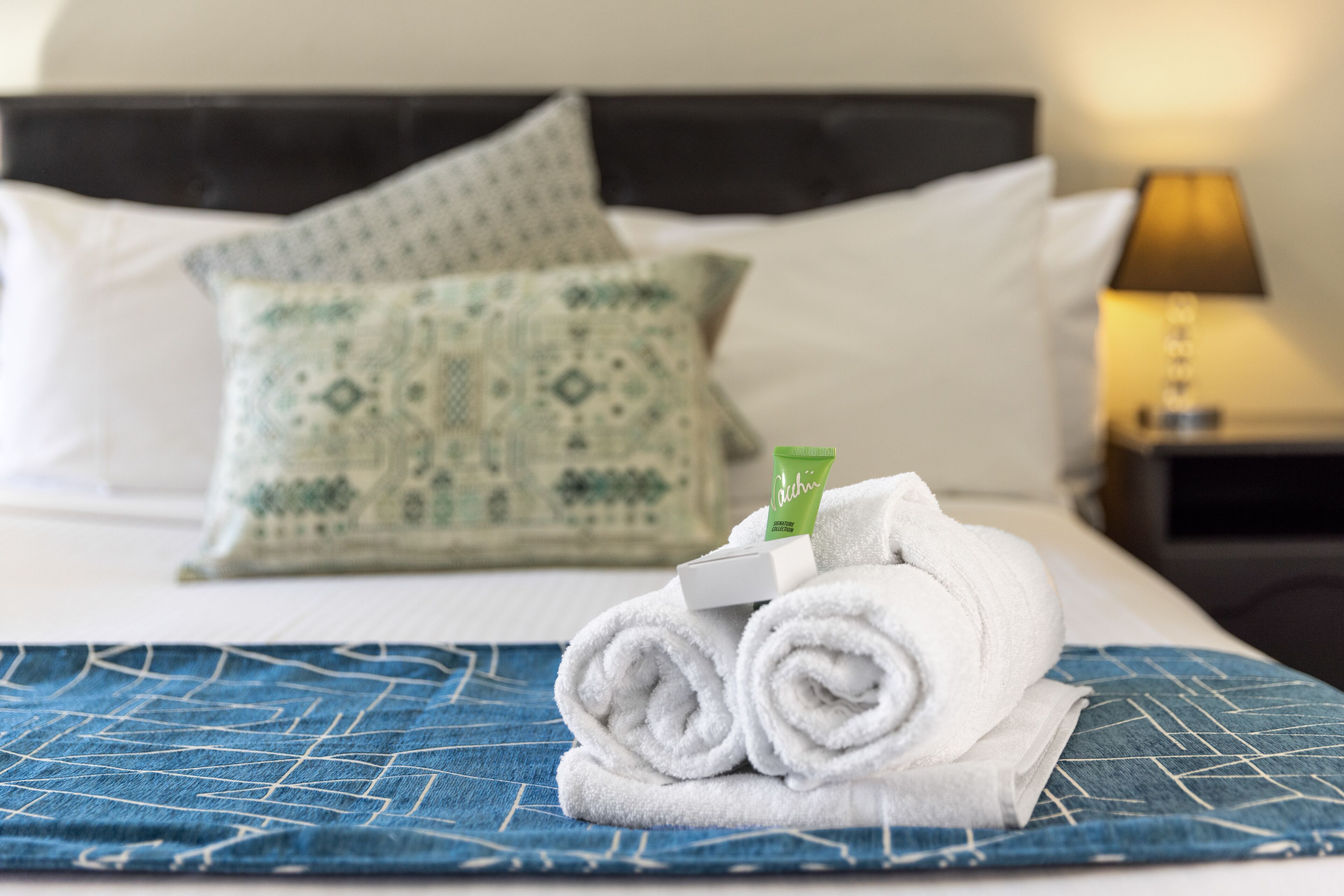 A neatly made bed with rolled white towels, a green pillow, and a white pillow.