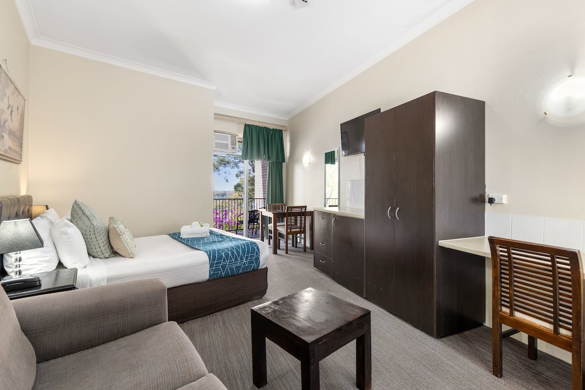 A hotel room with a bed, sofa, small table, and a kitchenette area.