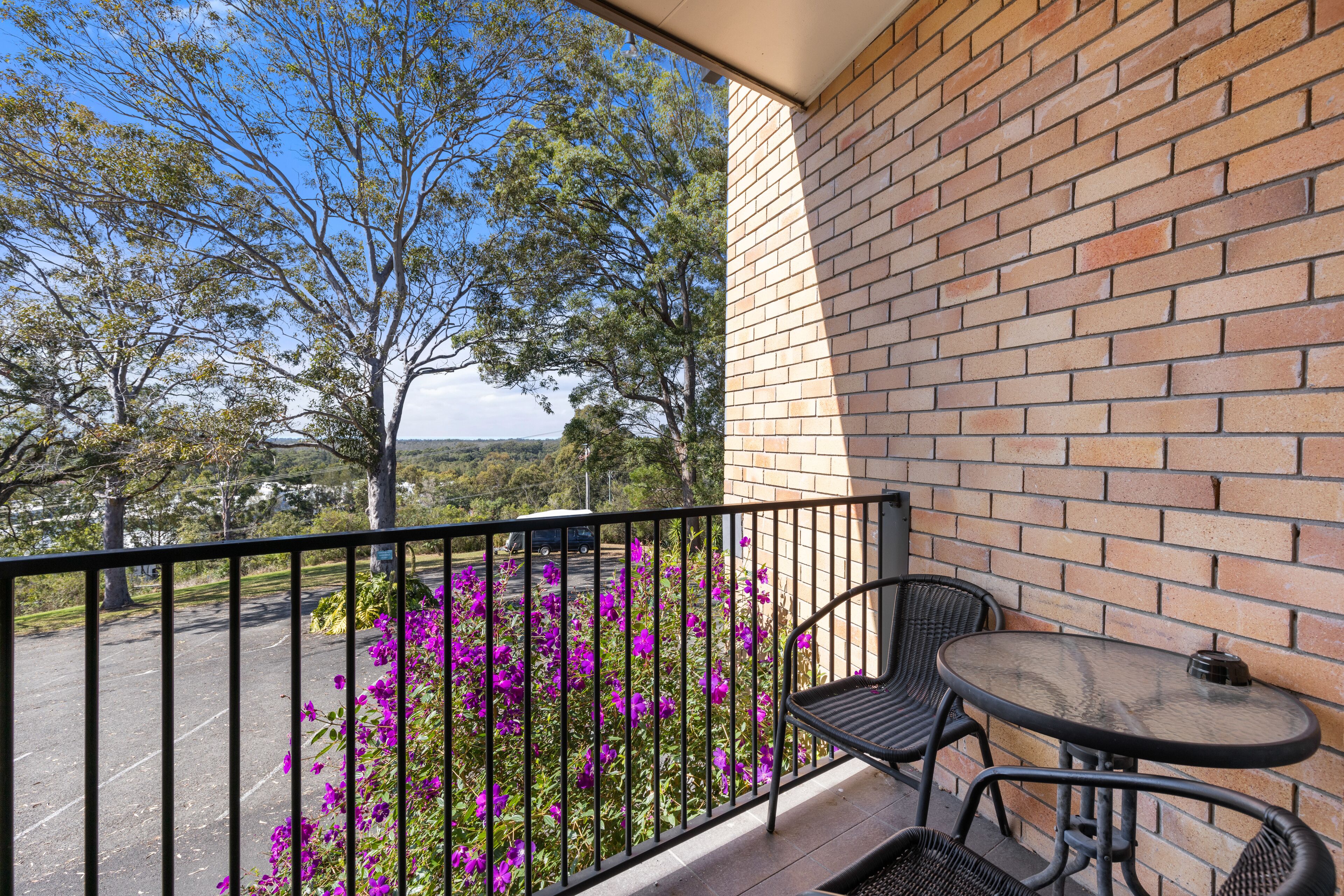 A balcony with a brick wall, a metal railing, and a table with two chairs.