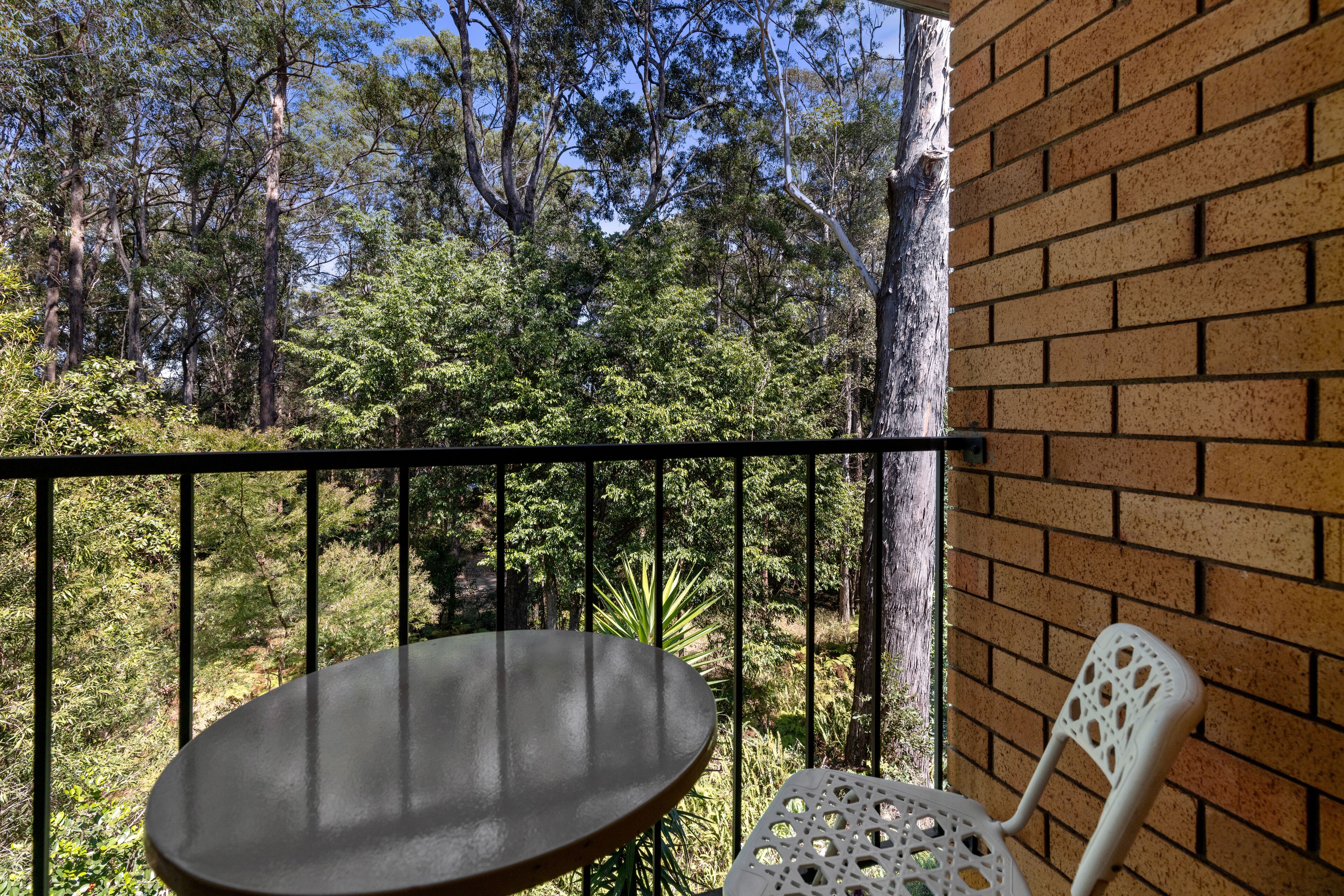 A balcony with a table and a chair, overlooking a forested area.